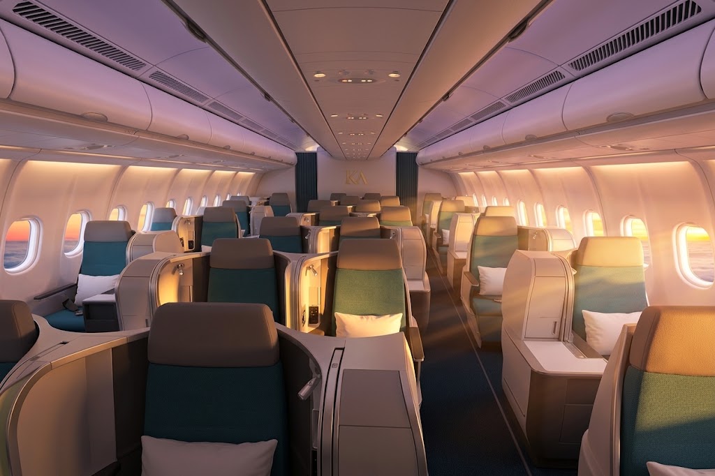 Airbus A330 business cabin with staggered lie-flat seats in teal upholstery and white pillows at sunset