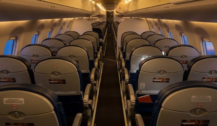 Embraer 190 cabin looking down the aisle, 2-2 grey seats with no seatback screens under evening lighting