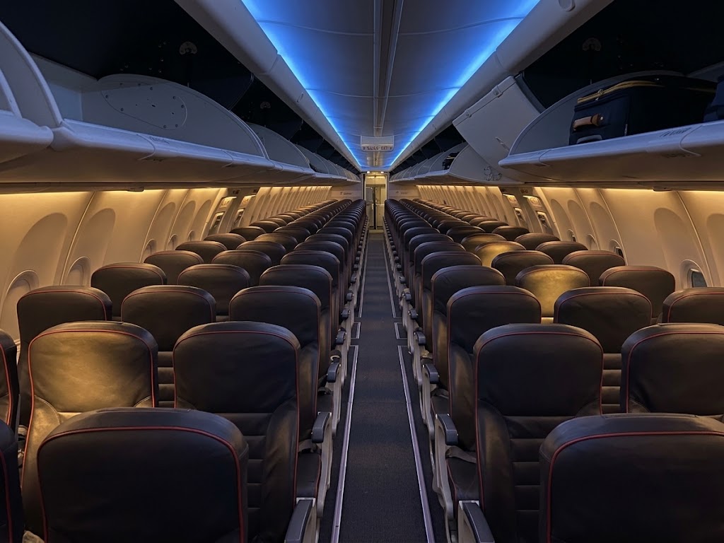 Arajet Boeing 737 MAX 8 cabin looking down the aisle, 3-3 dark leather seats with red piping under blue ceiling lighting
