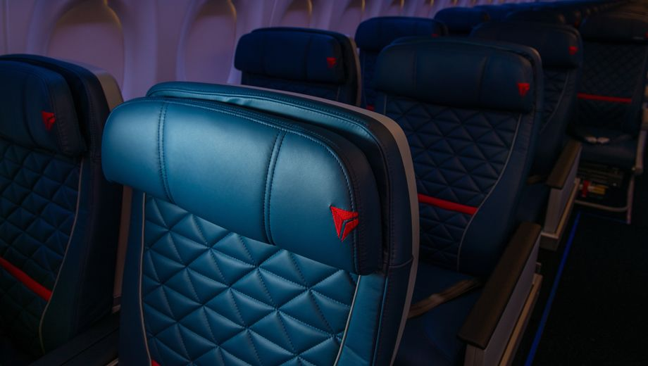 Delta A220-300 First Class cabin showing Collins MiQ recliner seats with quilted navy blue leather and red Delta logo accents