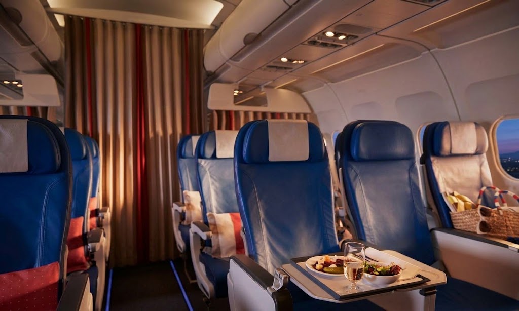 Narrowbody cabin with blue leather 3-3 seats, a meal on a tray table and a curtain dividing the cabin at dusk