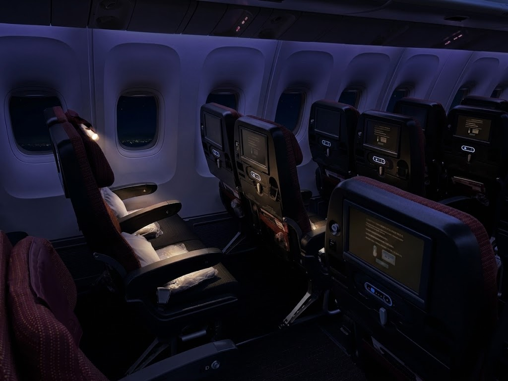 Japan Airlines Boeing 767-300ER economy cabin at night, seatback screens lit along the window line