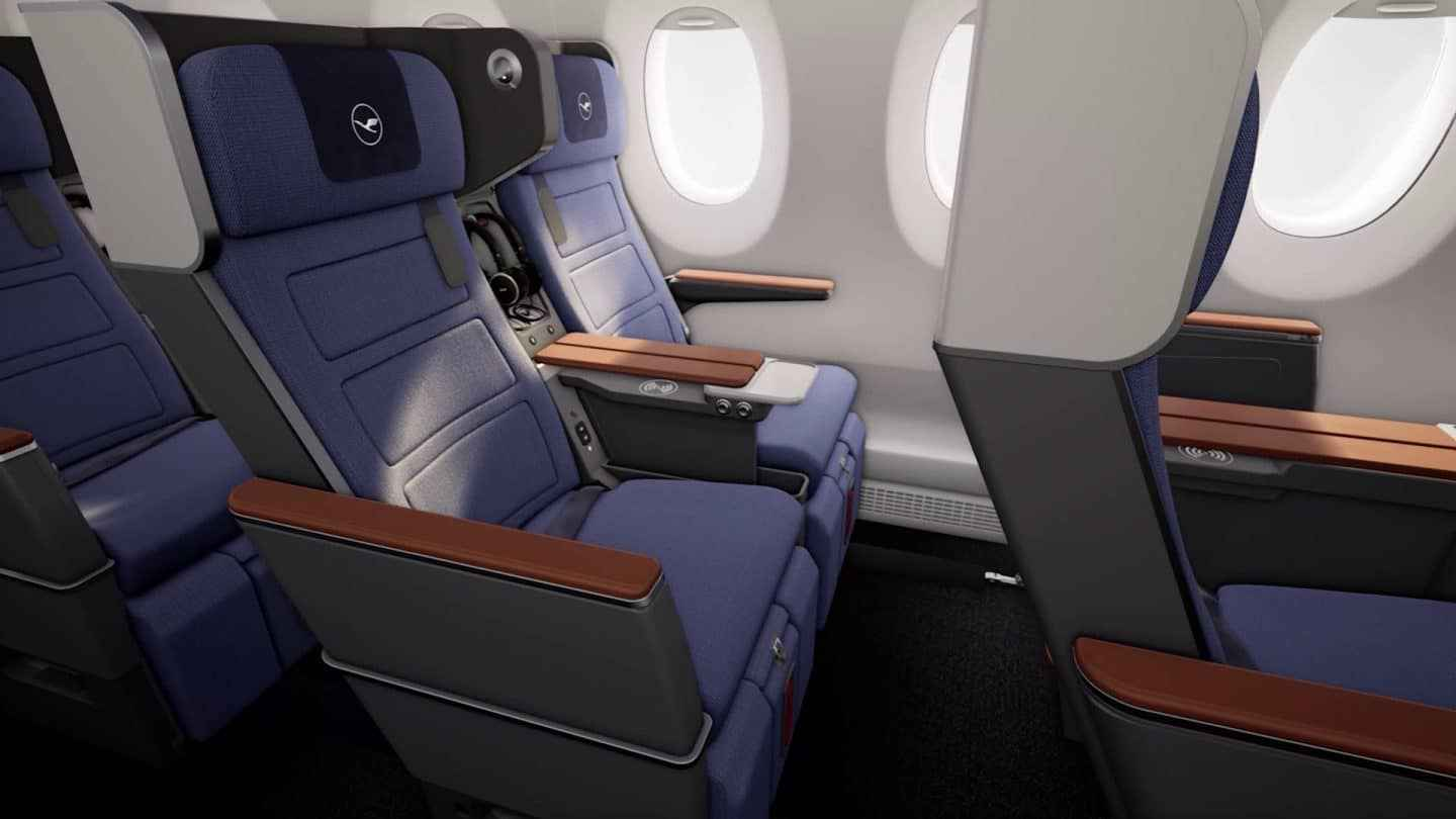 Lufthansa Allegris premium economy on the Airbus A350: blue shell-backed recliners with cognac leather armrests, winged headrests carrying the Lufthansa crane, and wireless charging in the centre console