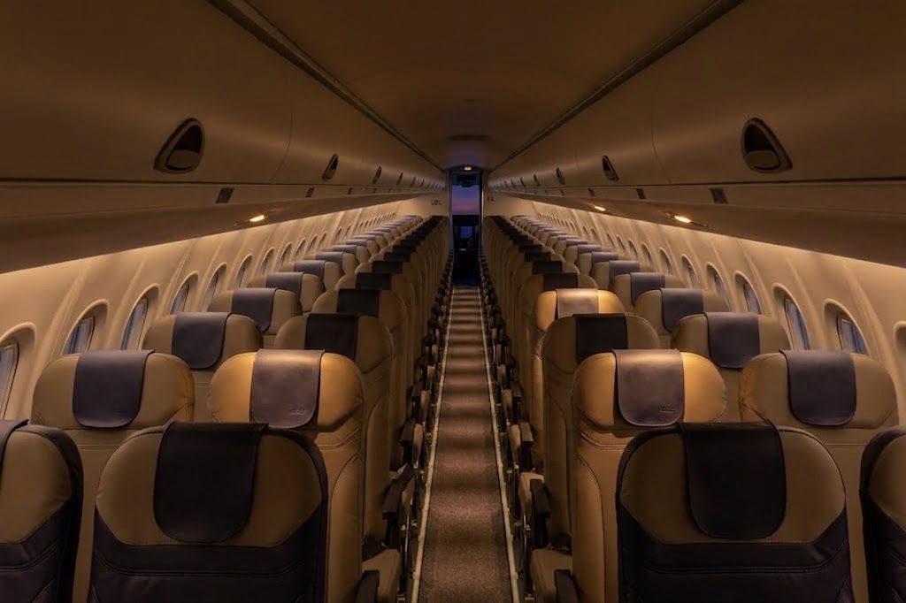 Porter Airlines Dash 8-400 cabin looking down the aisle, 2-2 tan leather seats with dark headrest covers under warm lighting