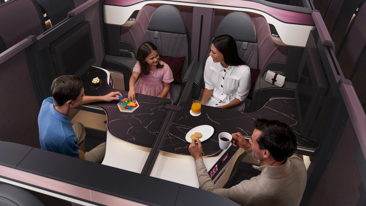 Four Qatar Airways Qsuite business class seats in the quad configuration, dividers lowered, with a family of four seated around the joined table