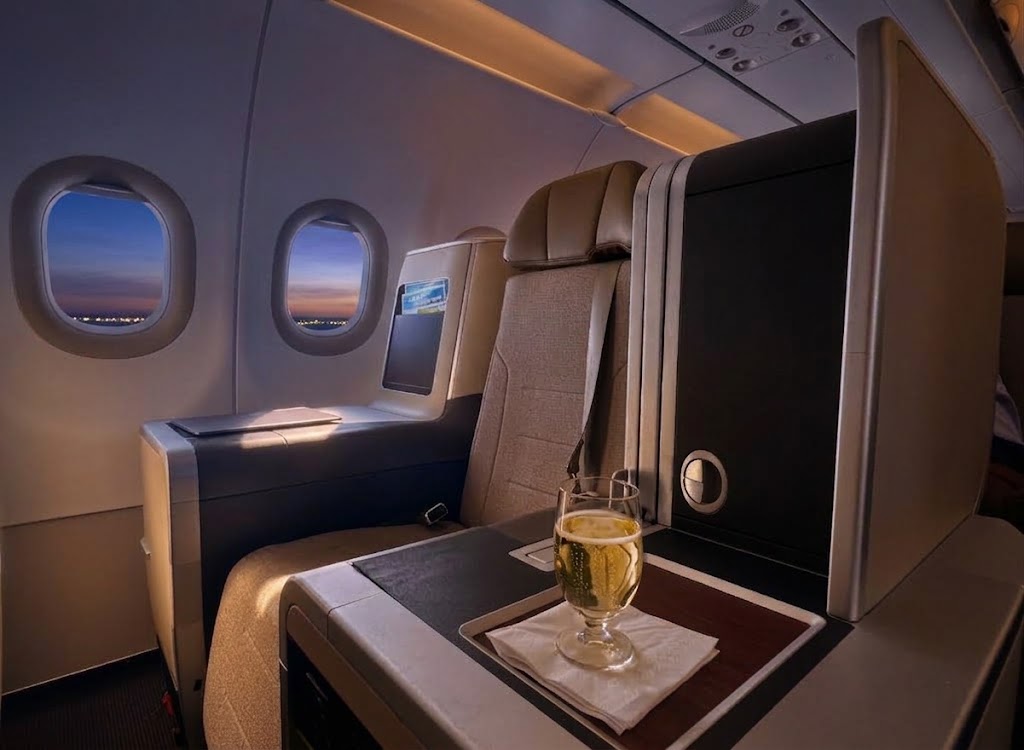 TAP Air Portugal Airbus A321LR business seat at dusk, lie-flat recliner in grey and tan with a glass of sparkling wine on the tray