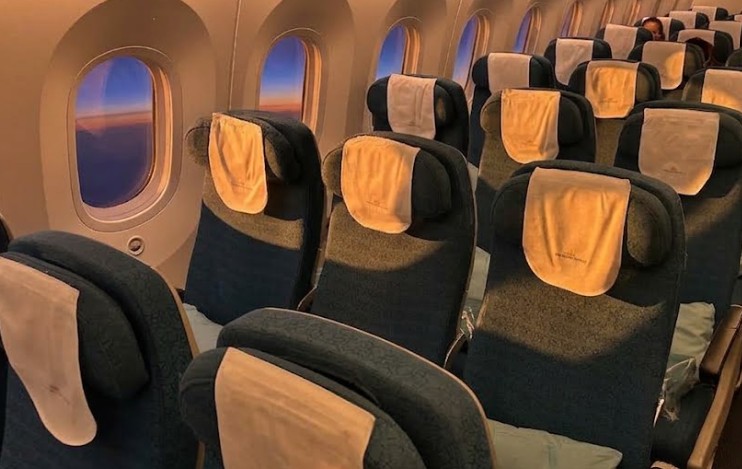 Vietnam Airlines Boeing 787-10 economy cabin, rows of blue-grey seats with cream headrest covers beside the windows at dawn