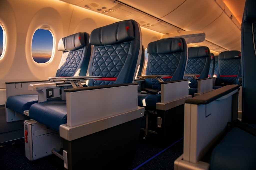 Delta A220-100 First Class cabin with quilted navy leather Collins MiQ recliners beside oversized windows at sunset