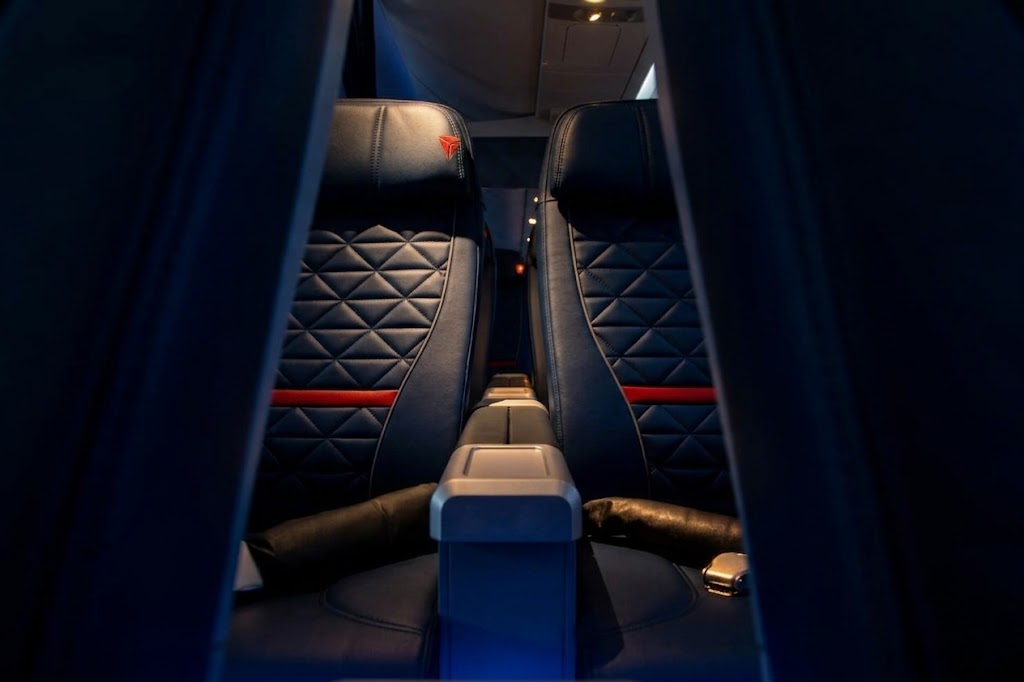 Delta A220-300 First Class pair of quilted navy leather Collins MiQ recliners seen through the cabin curtain