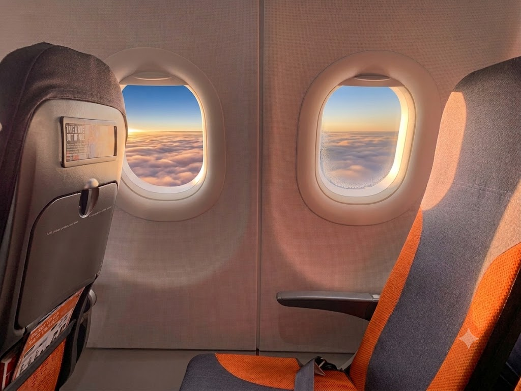 easyJet Airbus A319 economy window seats with orange upholstery and a sunset view over clouds