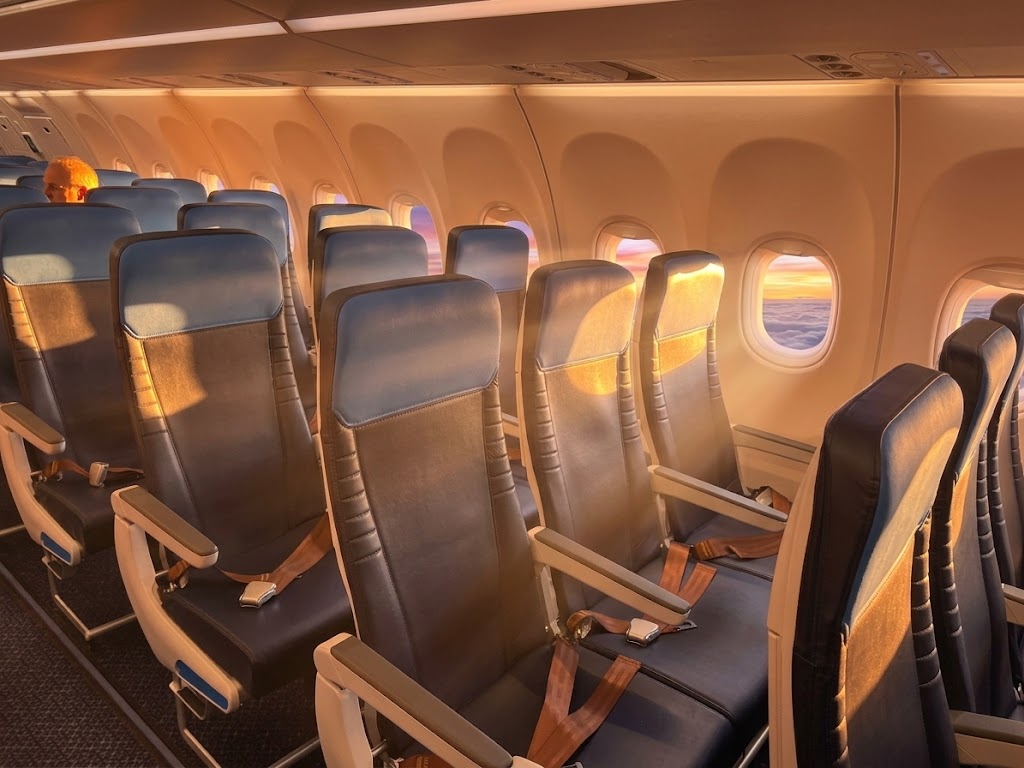 KLM Airbus A321neo economy cabin in 3-3 with blue and grey seats lit by low sun